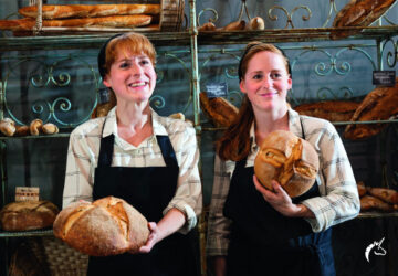 2 Frauen in einer Bäckerei halten Brot und lächeln.
