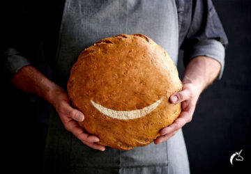 Bäcker hält ein Brot mit einem lachenden Mund.