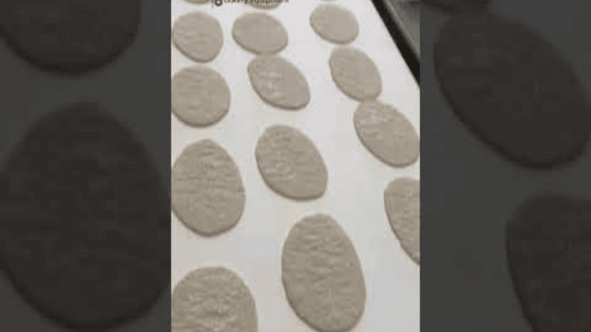 Several pieces of flattened, oval-shaped dough are arranged in rows on a white surface, likely prepared for baking.