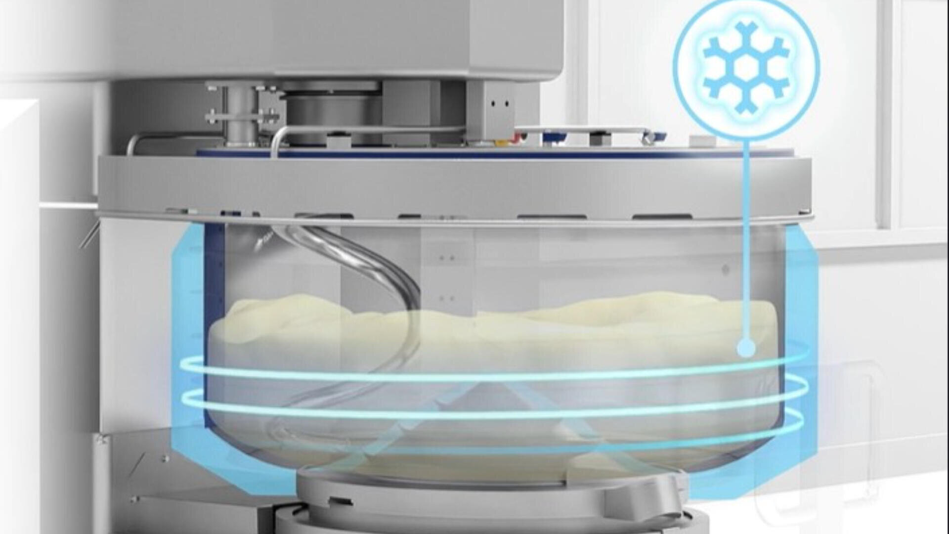 A close-up of a commercial dough mixer with a transparent bowl, showing dough inside. Blue glowing icons and lines indicate a cooling or refrigeration feature. The background shows part of a modern kitchen or bakery.