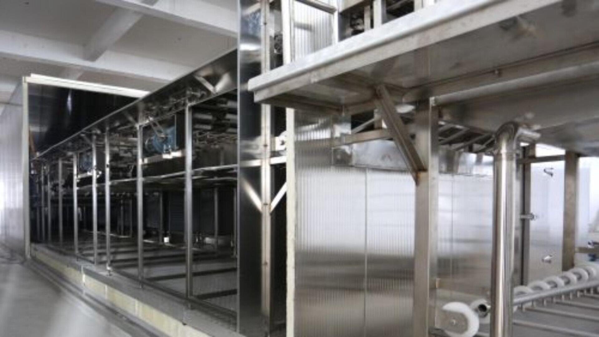 Eine große, industrielle Lebensmittelverarbeitungsmaschine aus Edelstahl in einer sauberen, geräumigen Anlage. Rohre, Förderbänder und verschiedene mechanische Komponenten sind in der Maschine zu sehen.