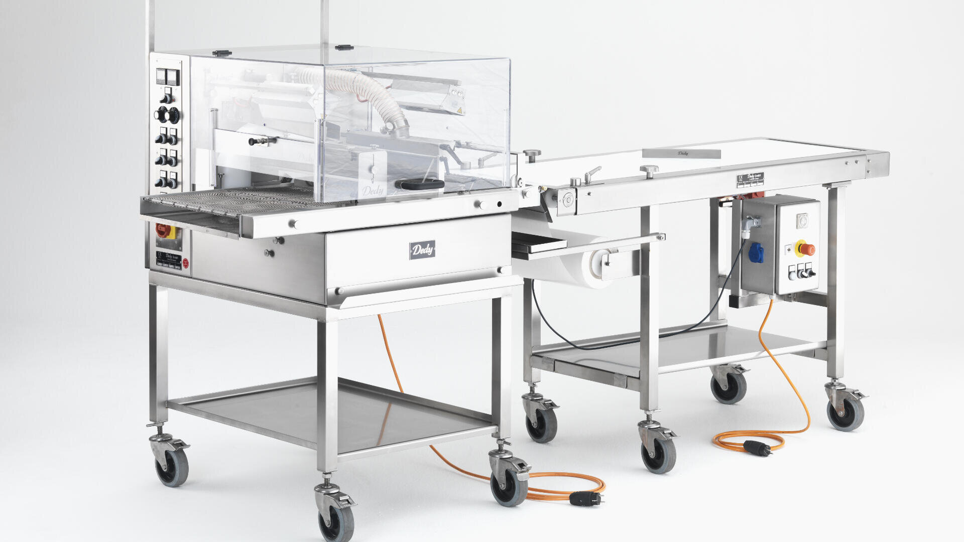 Eine gewerbliche Lebensmittelverpackungsmaschine aus rostfreiem Stahl mit durchsichtigen Kunststoffabdeckungen, Schalttafeln, Förderband und Laufrollen vor einem schlichten weißen Hintergrund. Orangefarbene Stromkabel sind in das Gerät eingesteckt.