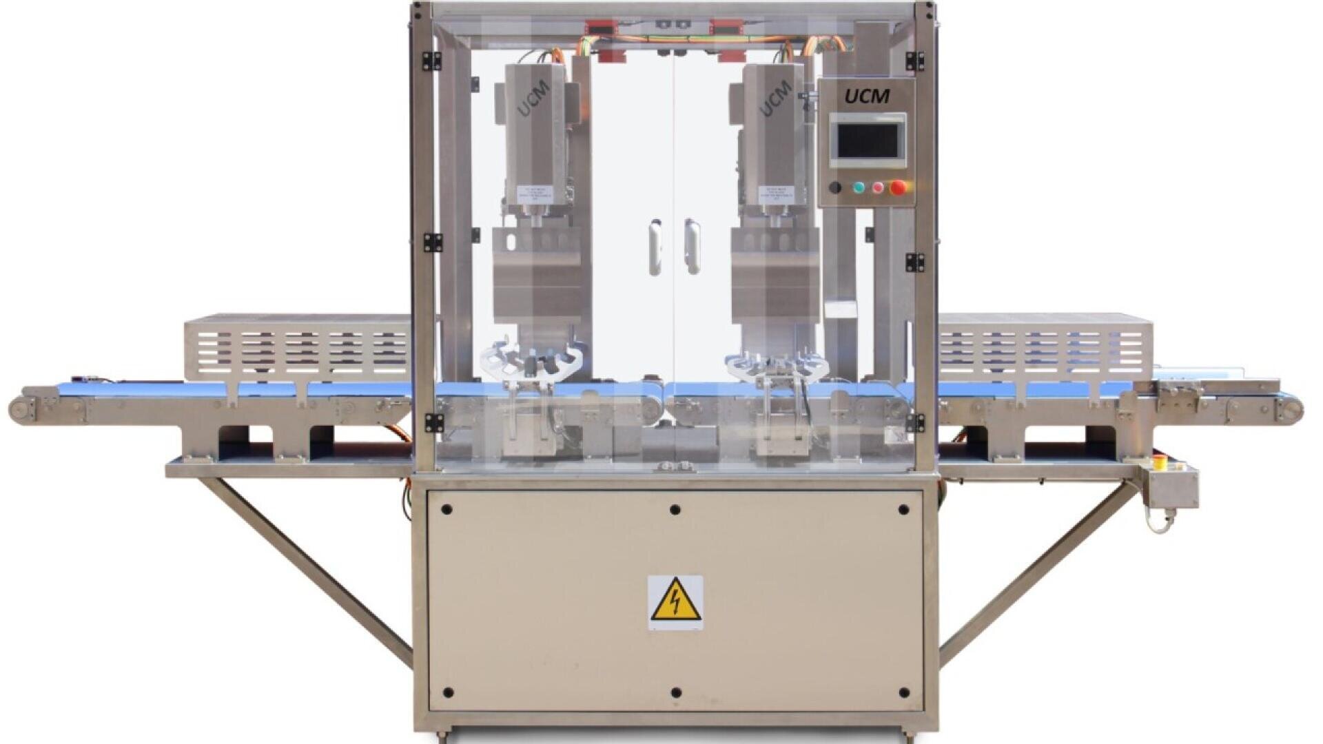 Vorderansicht einer Industriemaschine mit einem Bedienfeld und zwei Stationen, die durch transparente Platten abgedeckt sind, und einem Förderband, das durch die Maschine läuft. Auf der Frontplatte ist ein Warnschild angebracht.