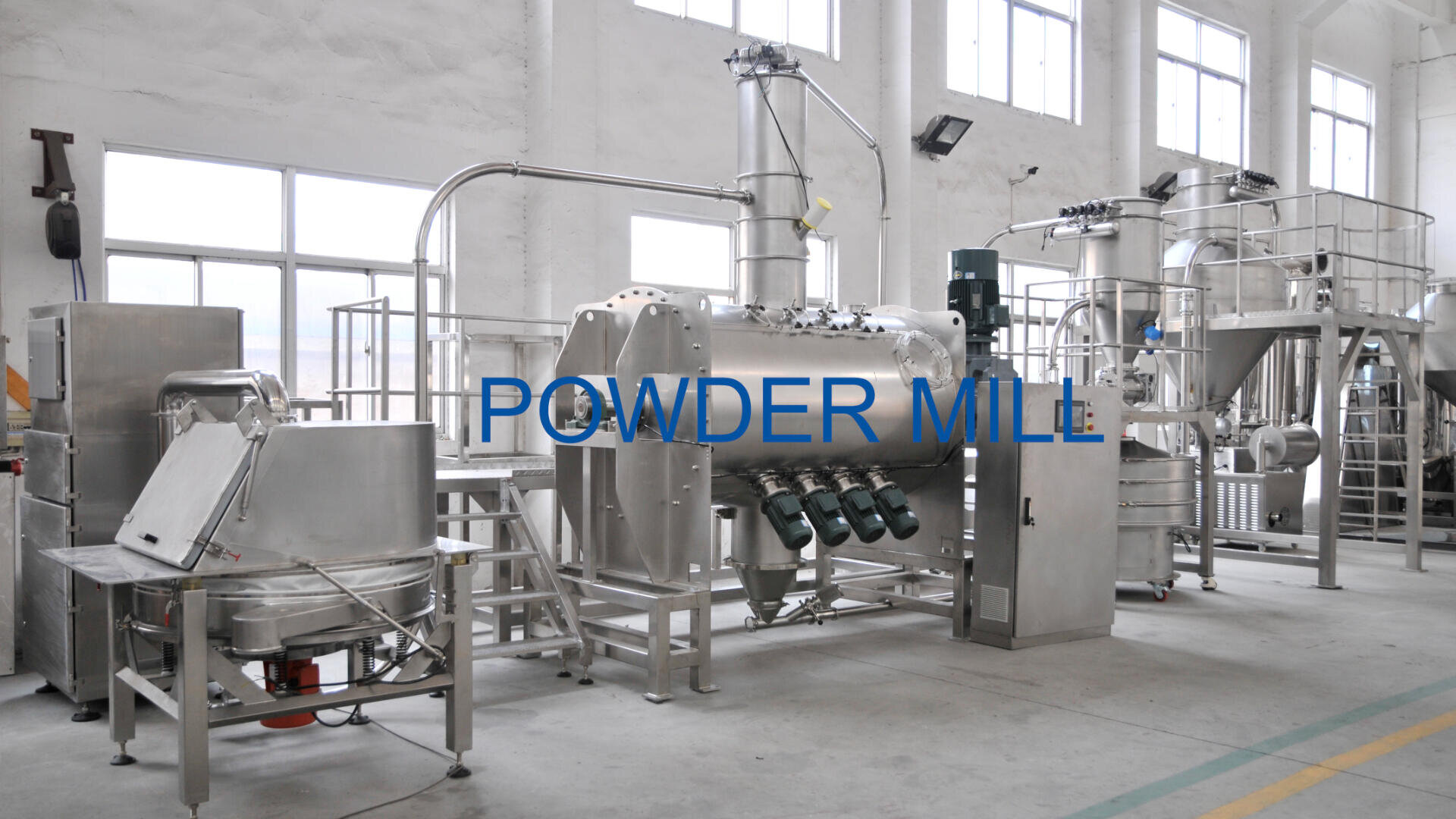 Industrial powder mill machinery in a clean, bright factory setting with various stainless steel equipment, pipes, and tanks. Blue text reading POWDER MILL is overlaid on the image.