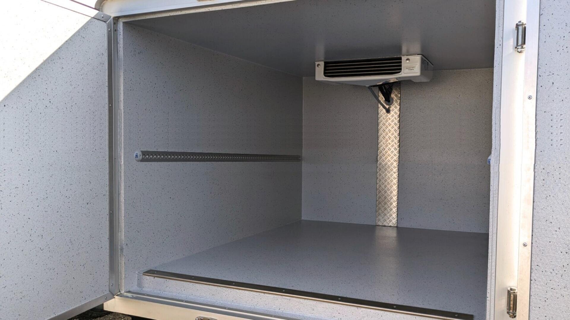 The image shows the empty interior of a refrigerated storage compartment with smooth, gray speckled walls and floor. A cooling unit is mounted on the ceiling near the back wall.