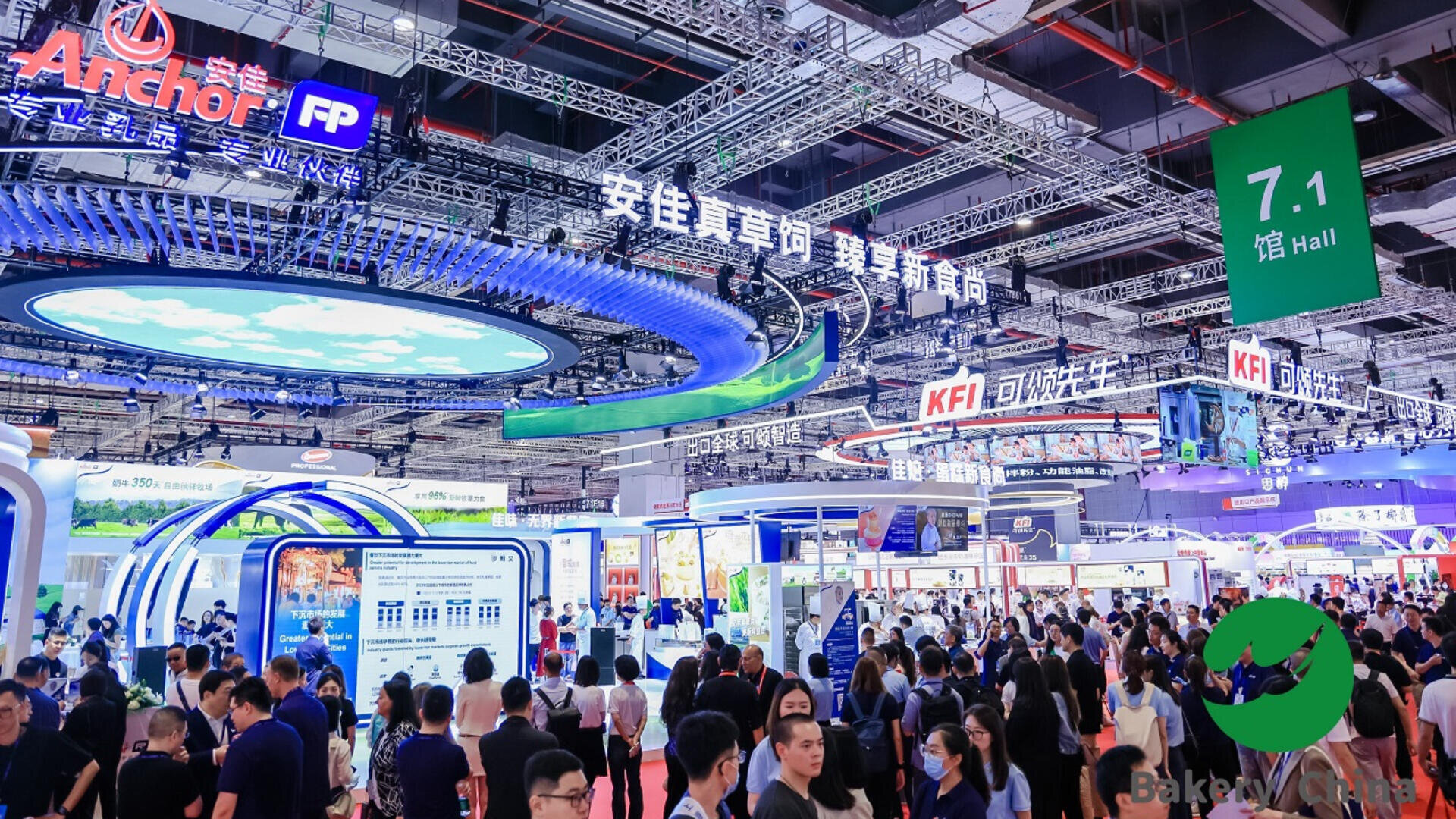 A large, crowded exhibition hall filled with people and illuminated booths, featuring bright signs in Chinese and English, curved digital displays, and overhead banners. The atmosphere is lively and bustling.