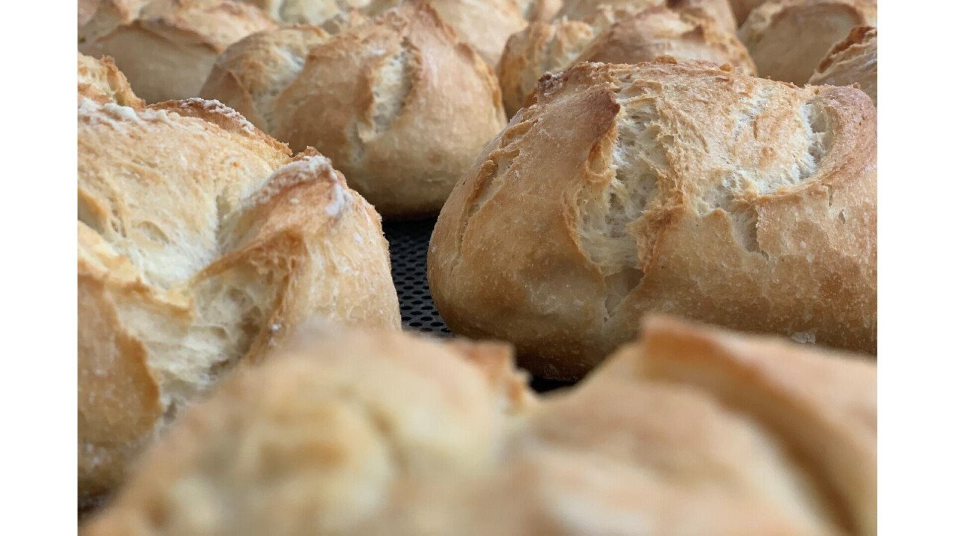 Close-up of several golden brown bread rolls with crispy, cracked crusts, arranged closely together on a baking tray.
