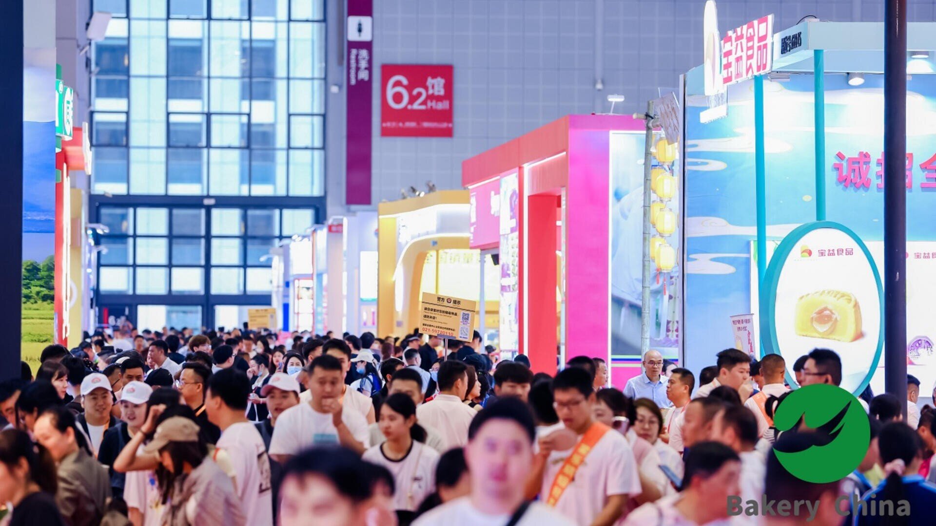 A large crowd of people walks through a busy exhibition hall with brightly colored booths and signs. The “Bakery China” logo is visible in the lower right corner.