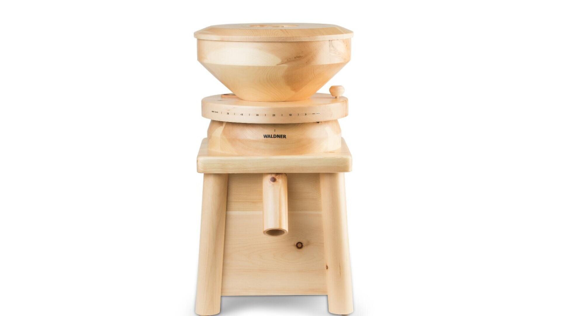 A wooden grain mill with a round hopper on top, a circular grinding section in the middle labeled Waldner, and a spout at the bottom, all standing on four sturdy legs.