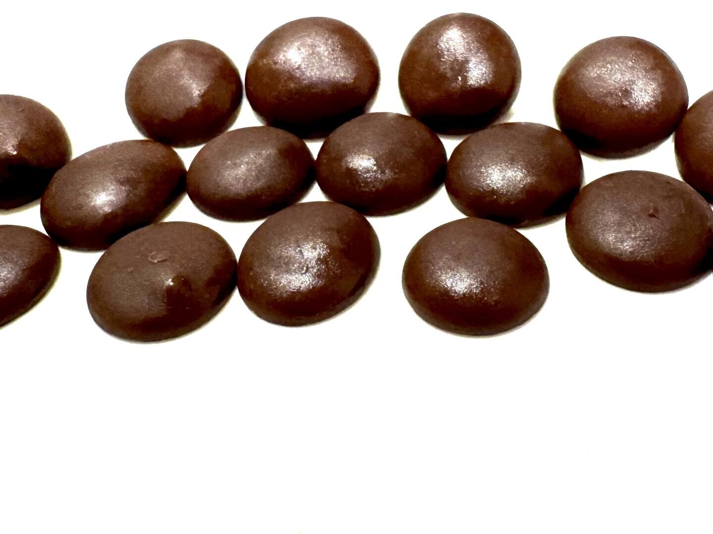 Fourteen round, shiny chocolate candies are arranged on a white background, with most of them touching or slightly overlapping each other.