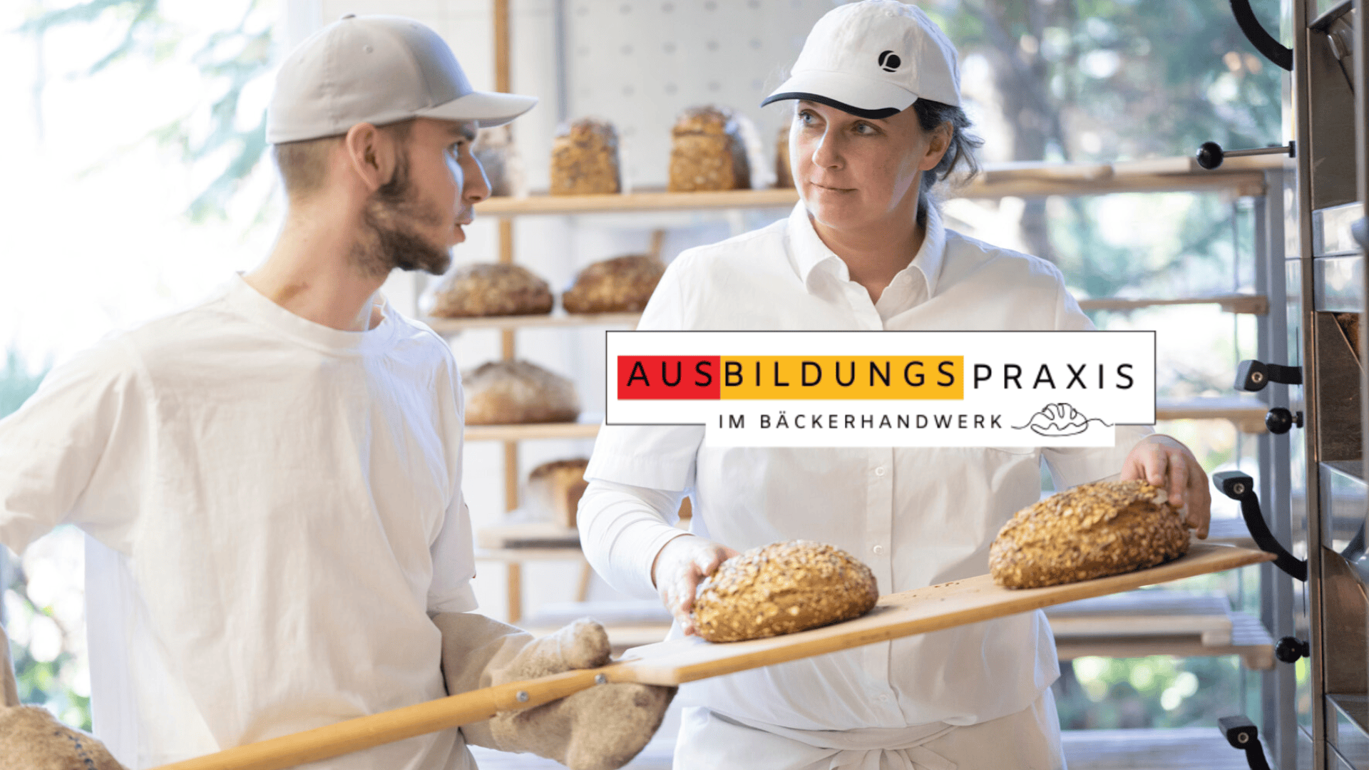 Zwei Bäcker in weißen Uniformen legen frisch gebackene Brotlaibe auf ein Gestell. Das Logo "AUSBILDUNGSPRAXIS IM BÄCKERHANDWERK" ist überlagert und wirbt für die Ausbildung im Bäckerhandwerk.