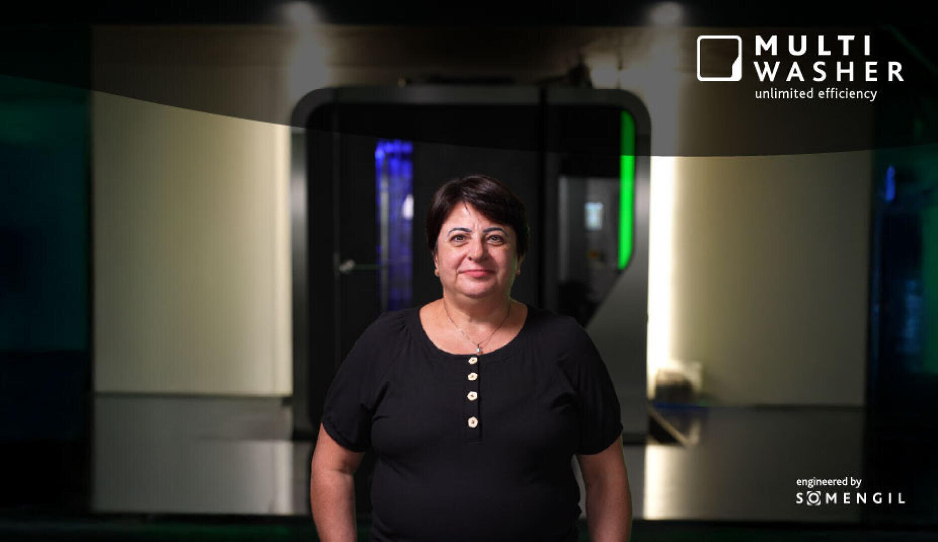 A woman with short dark hair, wearing a black buttoned shirt, stands indoors in front of a modern industrial machine. The text MULTI WASHER unlimited efficiency and engineered by SOMENGIL appears in the top right corner.