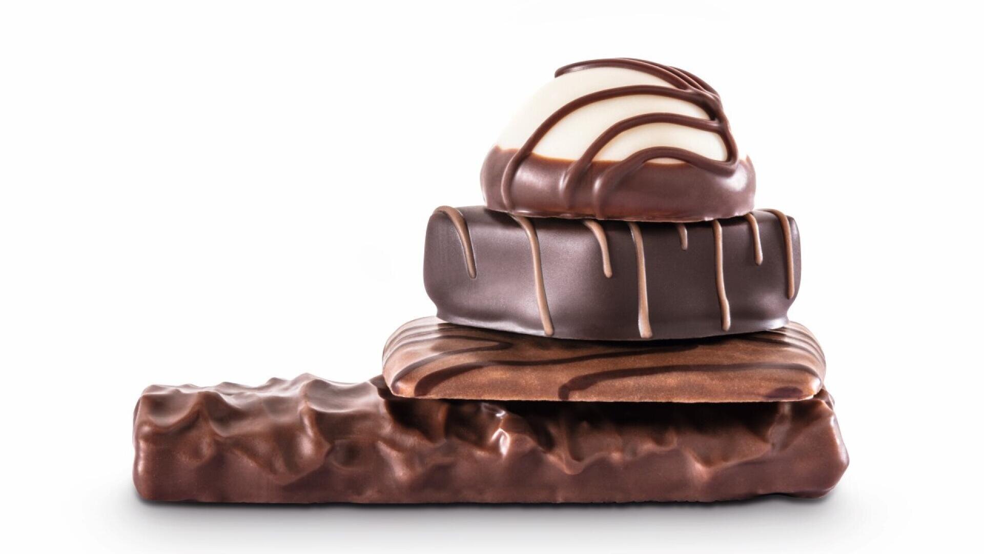 A stack of four assorted chocolate candies with different shapes and drizzles, arranged against a white background.