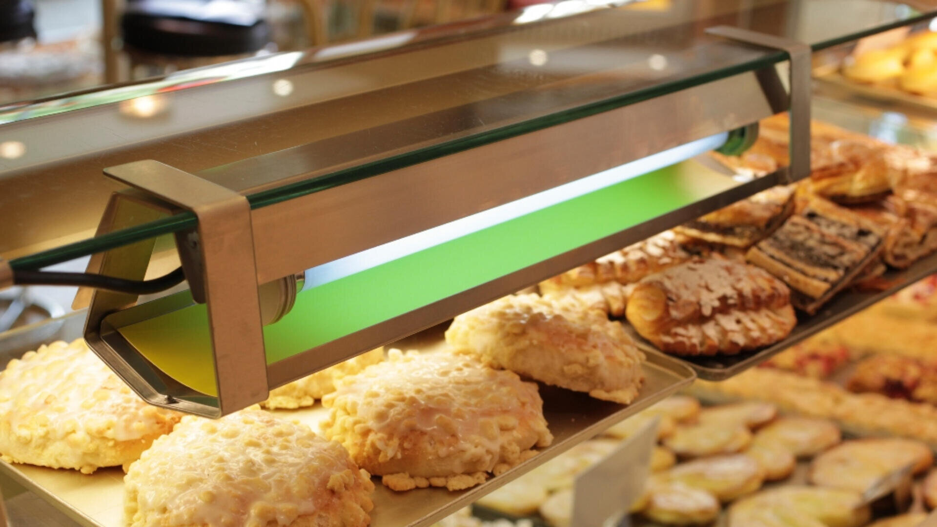 Eine Bäckereivitrine, gefüllt mit verschiedenen Backwaren, darunter Eis- und Streuselkuchen, beleuchtet von einem grün-weißen Oberlicht.