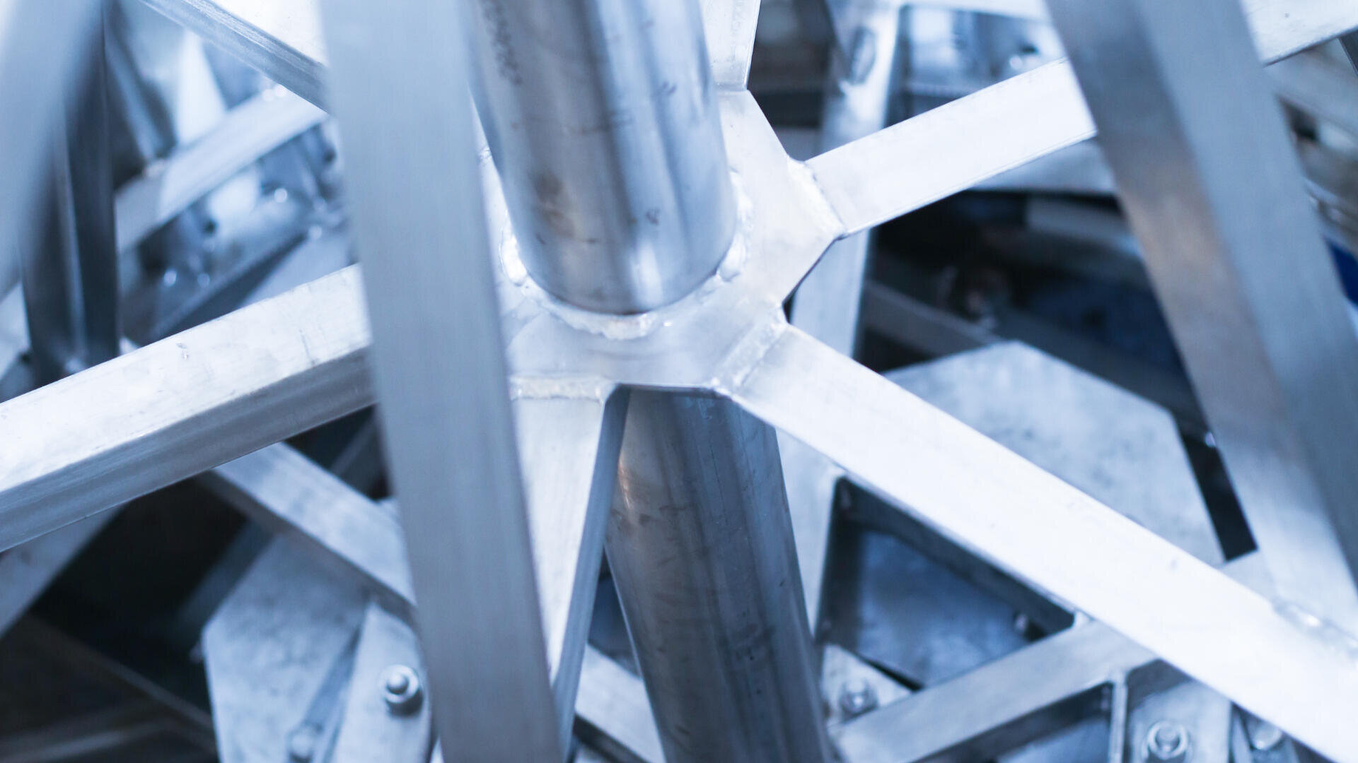 Close-up of an abstract arrangement of intersecting metal beams and rods, creating a geometric pattern with a silvery-blue tone.