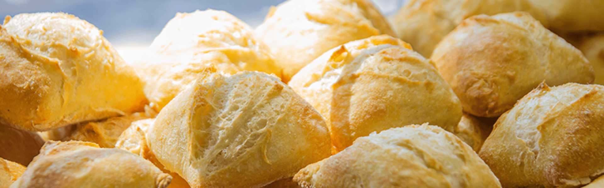 Eine Nahaufnahme mehrerer goldbrauner Brötchen, frisch gebacken, mit knuspriger, strukturierter Kruste, übereinander gestapelt und von natürlichem Licht angestrahlt.