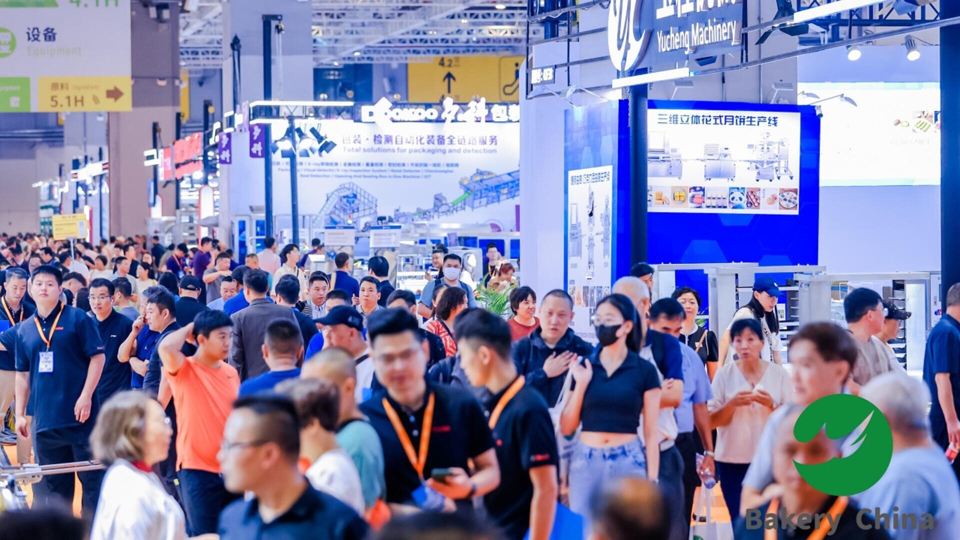A large crowd of people attends an indoor trade show or exhibition with bright lights, booths, and signs. Most attendees wear casual clothing, and some wear face masks. The Bakery China logo is visible in the corner.