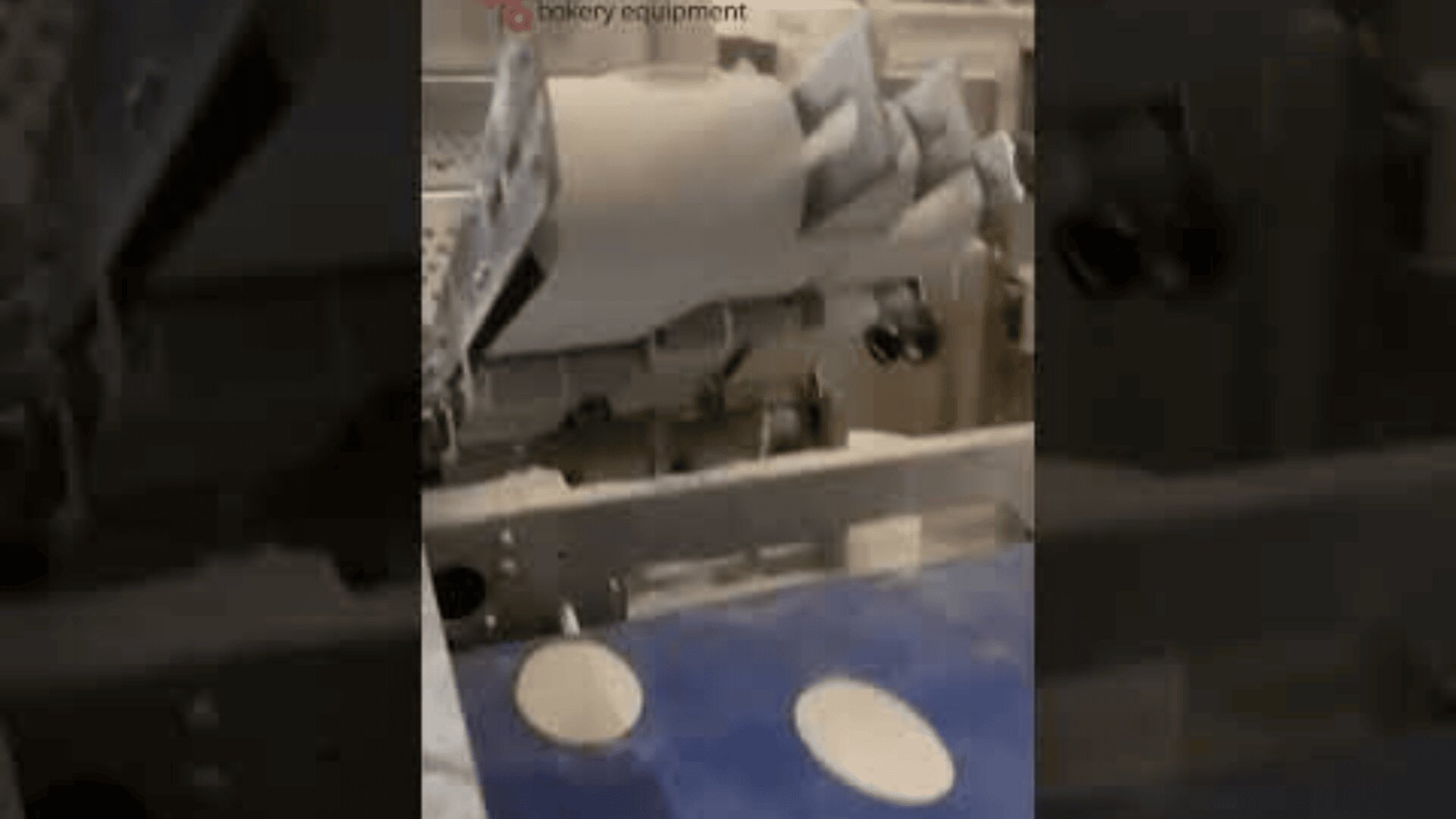 Eine Maschine in einer Bäckerei schneidet auf einem Förderband runde Teigformen aus einer großen Platte.