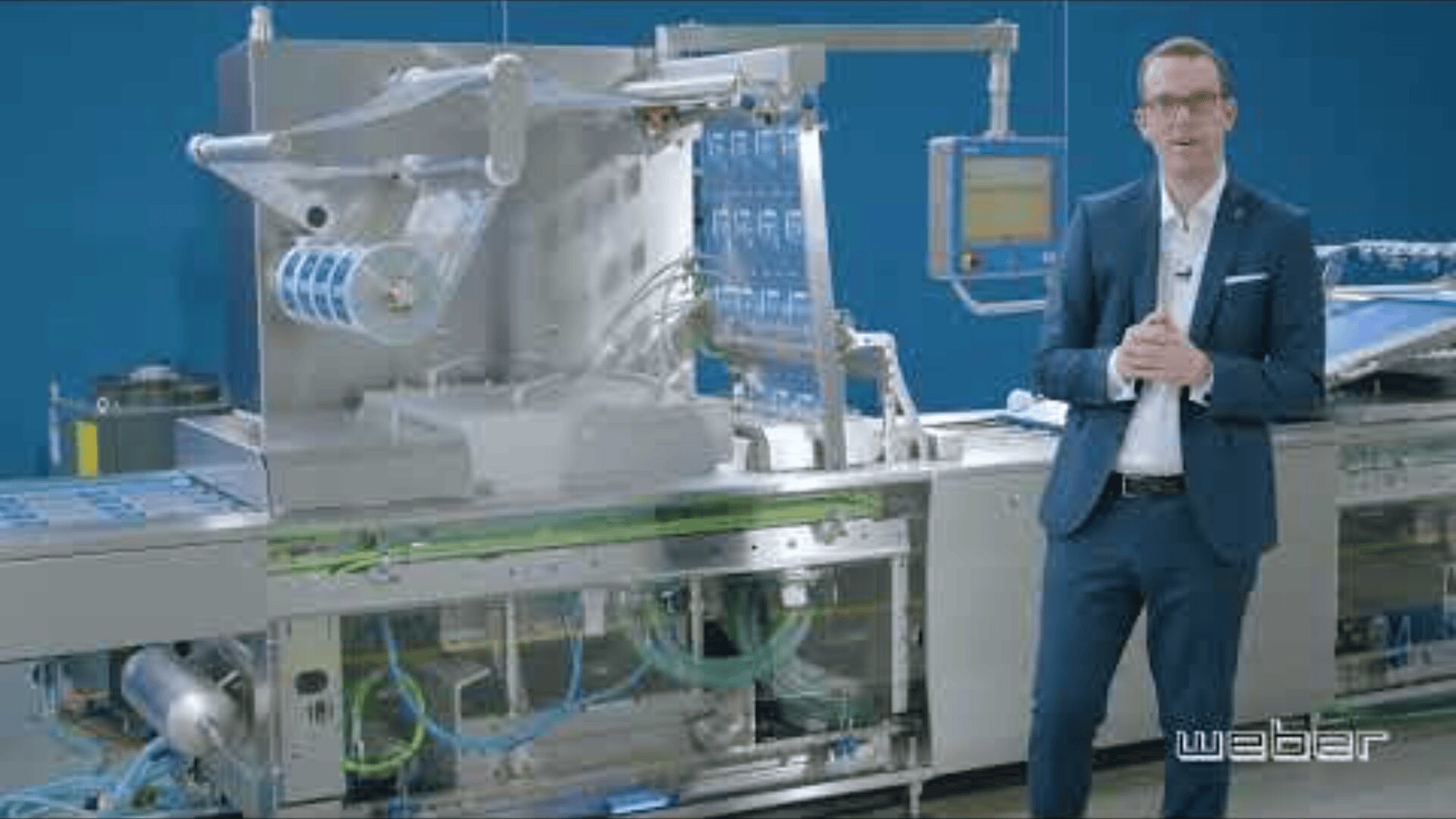 A man in a suit stands next to industrial packaging machinery with blue accents and a digital control panel, set against a blue background. The brand name webar appears in the bottom right corner.