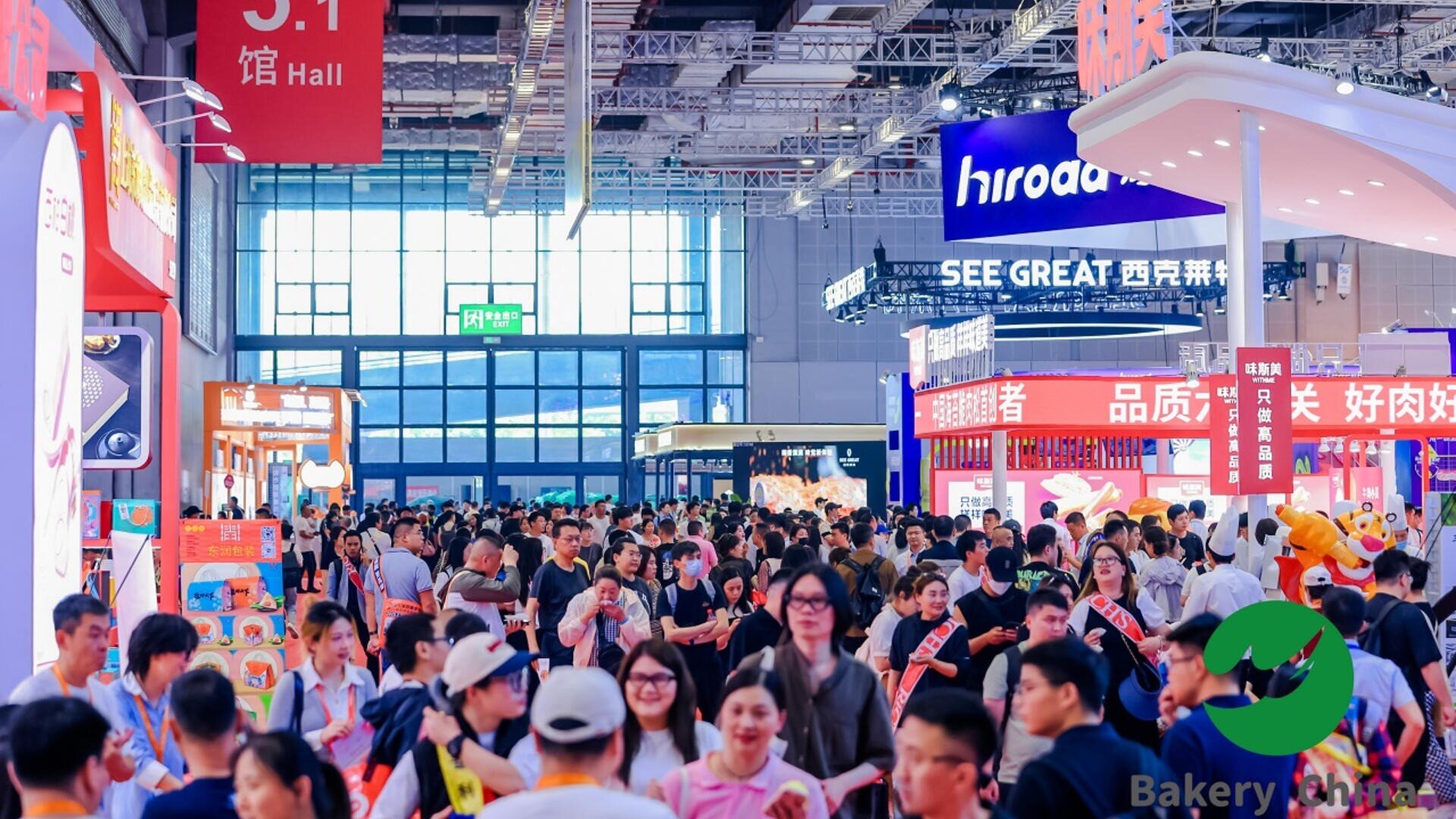 A large crowd of people walks through a busy indoor exhibition hall, surrounded by brightly colored booths and signs in Chinese. The scene is lively, with many attendees exploring the event.