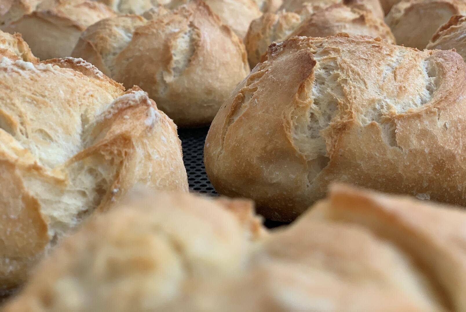 Nahaufnahme von mehreren goldbraunen Brötchen mit knuspriger, strukturierter Oberfläche, die dicht nebeneinander auf einem Backblech liegen.