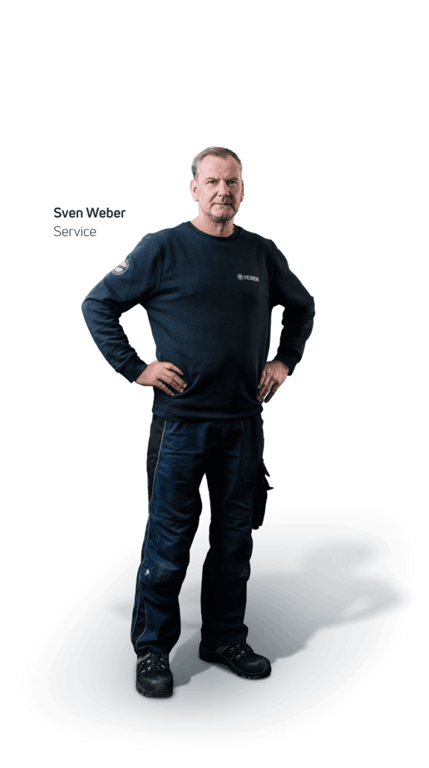 Ein Mann in einem marineblauen langärmeligen Hemd und einer dunkelblauen Arbeitshose steht mit den Händen in den Hüften und schaut in die Kamera. Das Hemd hat ein Logo auf der Brust. Der Text lautet Sven Weber Service.