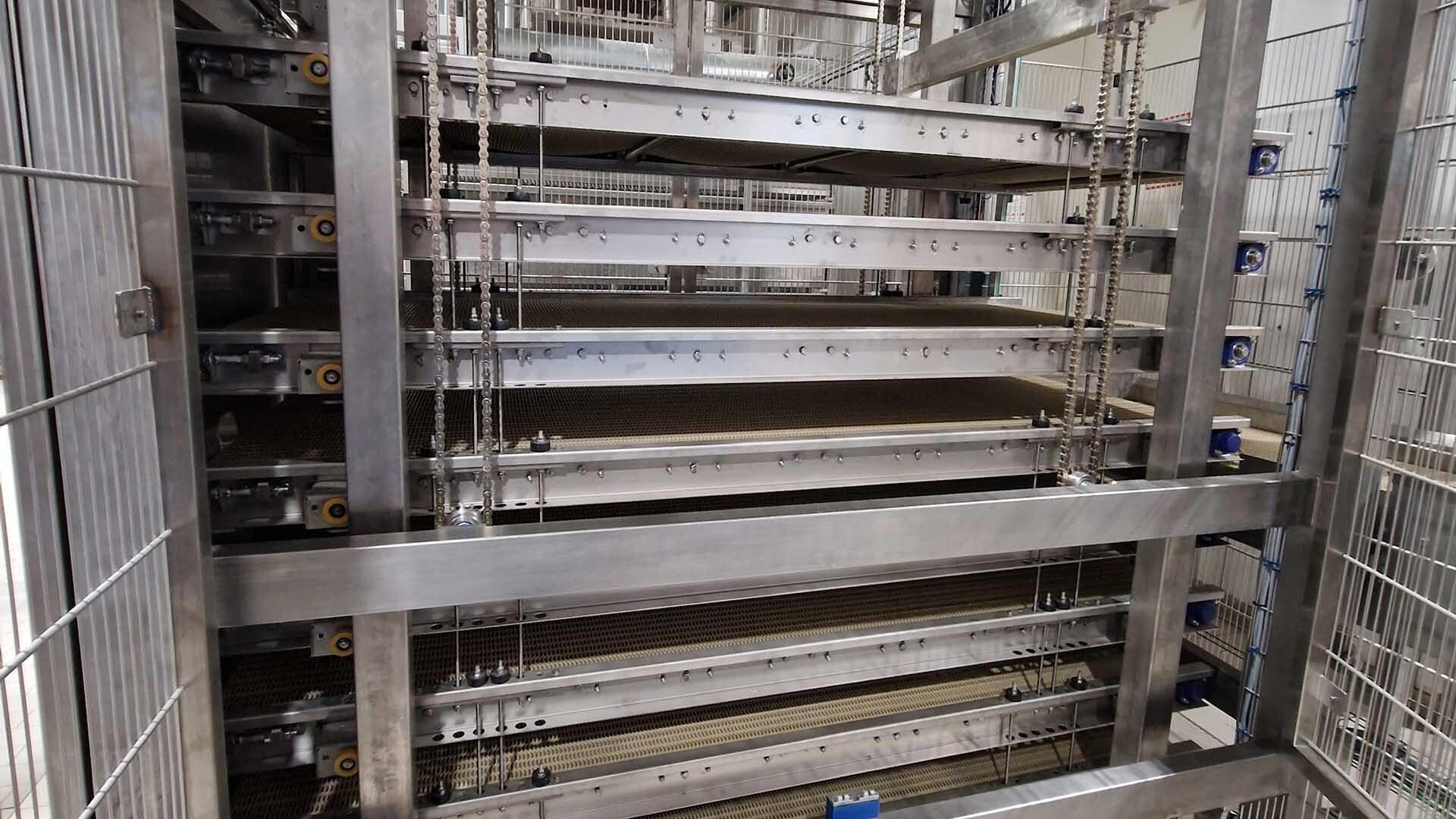 Nahaufnahme einer mehrstöckigen Metallstruktur mit Förderbändern aus Maschendraht innerhalb eines Käfigs, wahrscheinlich Teil einer industriellen oder landwirtschaftlichen Verarbeitungsanlage.