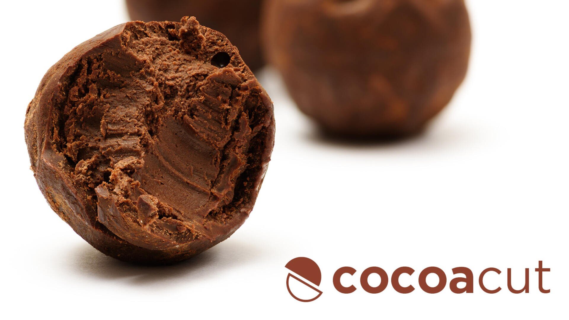 Nahaufnahme einer Schokoladentrüffel mit rauer, strukturierter Oberfläche. Im Hintergrund ist eine weitere Trüffel unscharf. Rechts ist das Logo „Cocoacut“ mit einem Kakaobohnen-Symbol zu sehen.