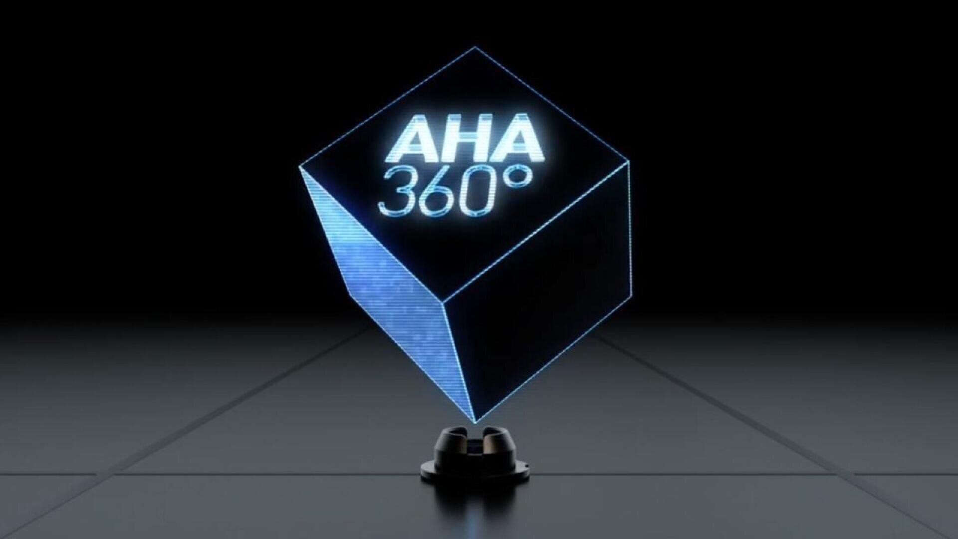 A glowing, blue holographic cube hovers above a small black base. The words AHA 360° are displayed on the cube. The background is dark with a reflective surface and subtle grid lines.