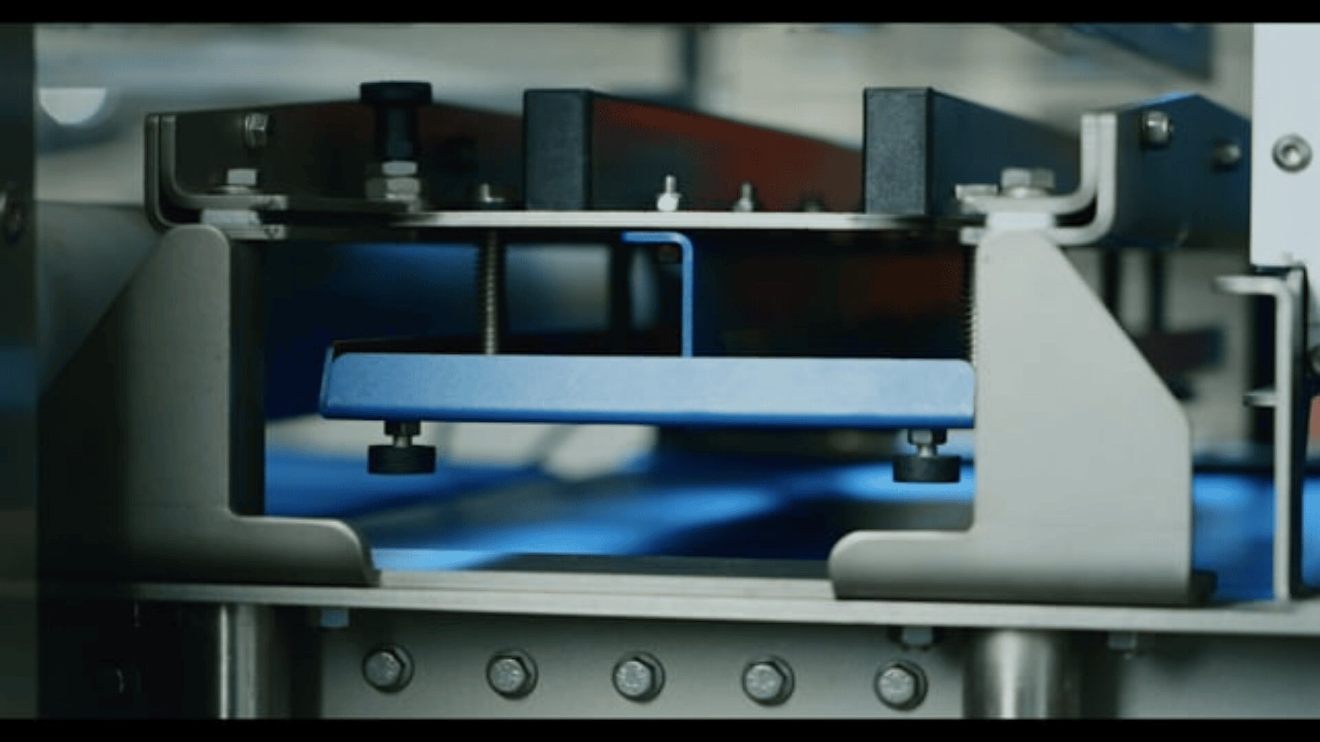 Close-up of industrial machinery with metal and blue components, showing bolts, screws, and mechanical parts, possibly part of a manufacturing or assembly line process.