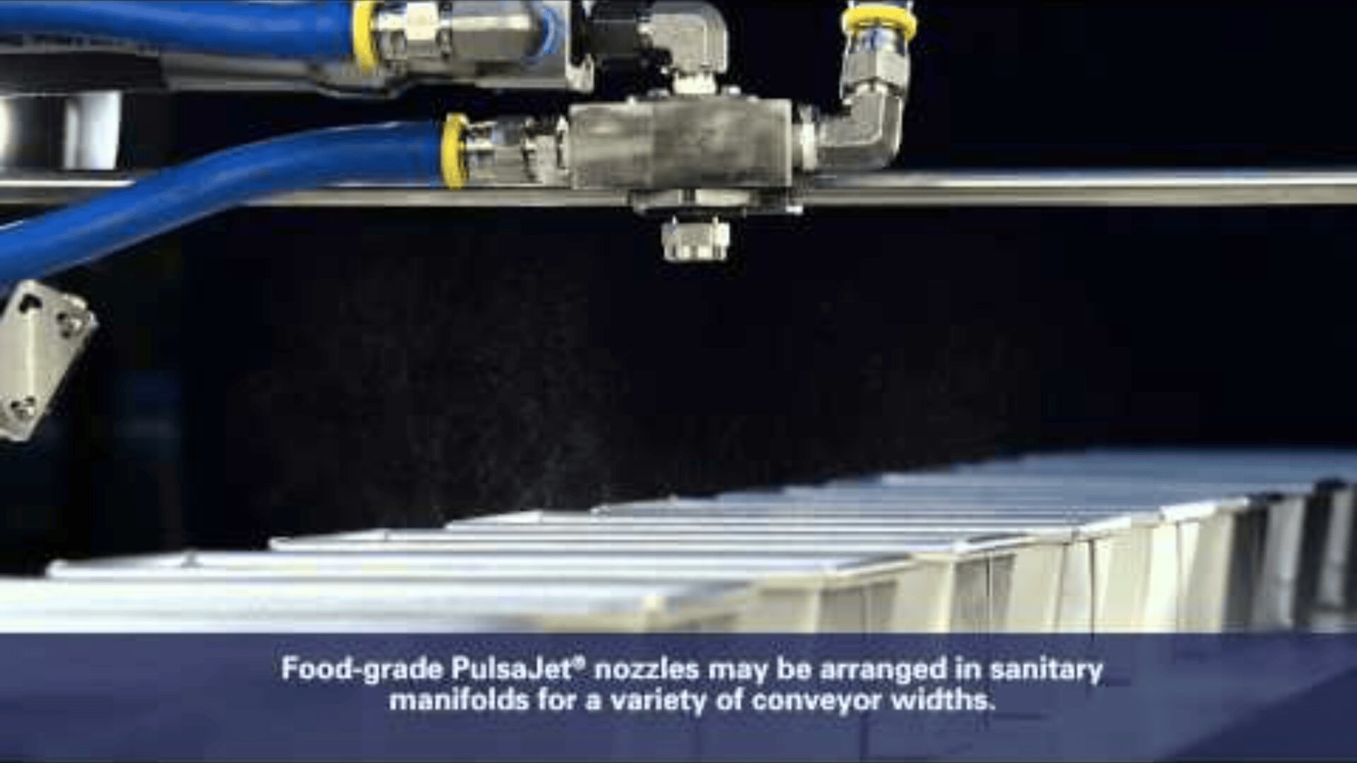 Close-up of a food-grade PulsaJet® nozzle spraying mist over a row of containers on a conveyor belt. Blue tubing is attached to the nozzle. Caption below describes sanitary manifold arrangements for various conveyor widths.