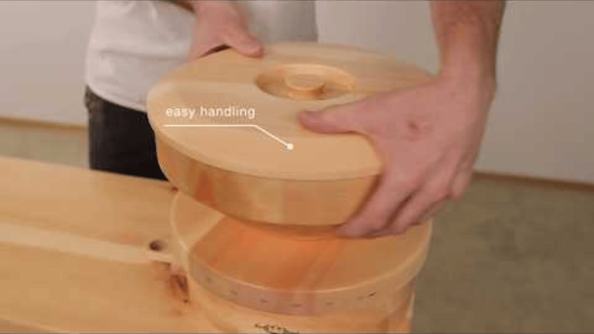 A person lifts the wooden lid of a round container. An arrow with the text easy handling points to the lid, highlighting its ergonomic design for simple use.