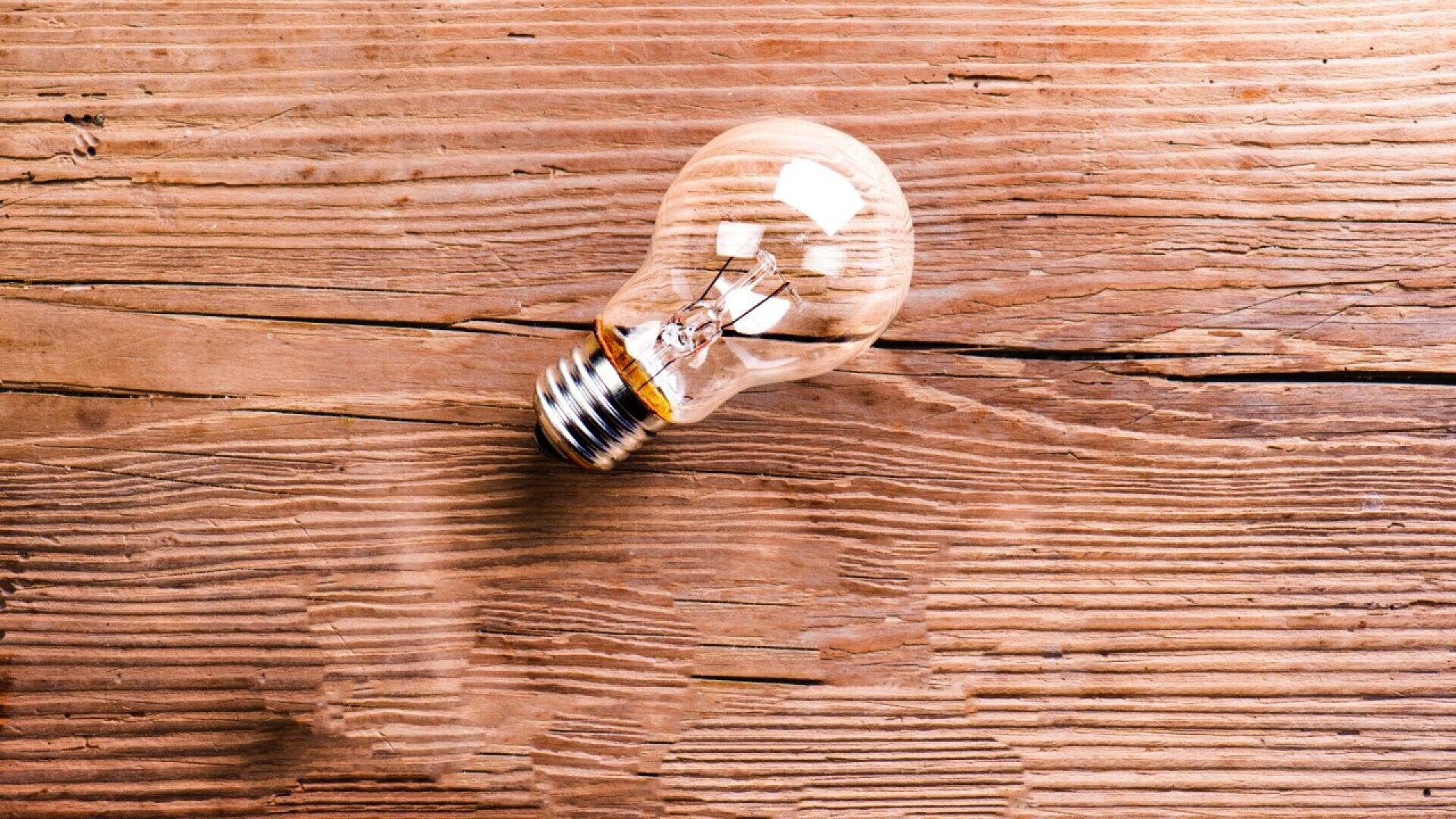 A clear incandescent light bulb lying on its side on a rustic wooden surface with visible grain and texture.