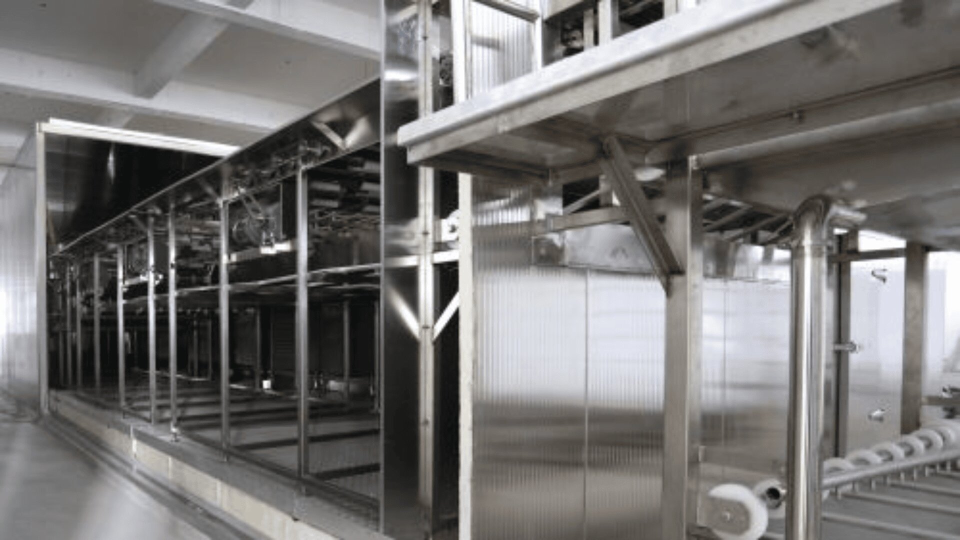 A large, industrial stainless steel food processing machine with multiple compartments and conveyor belts inside a factory setting. The equipment is clean and shiny, reflecting the orderly environment.