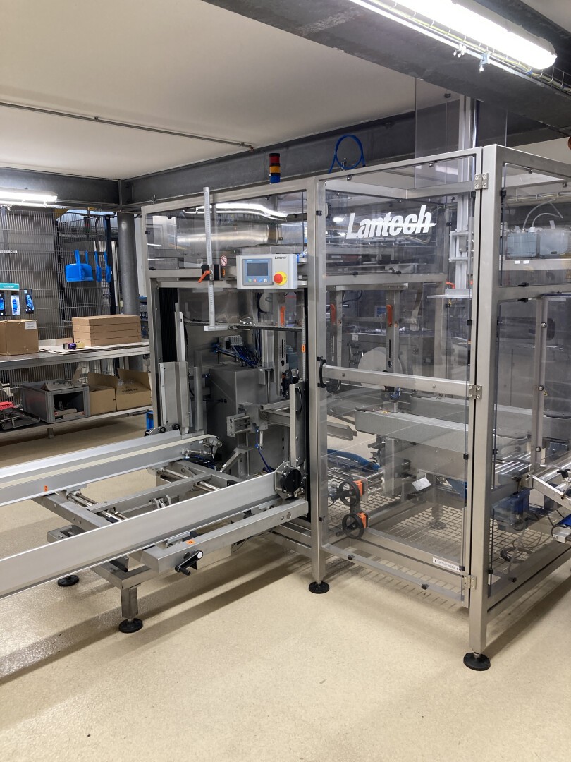 A large, industrial packaging machine with the brand name Lamitech displayed, located in a clean, well-lit factory setting with conveyor belts and various controls visible.