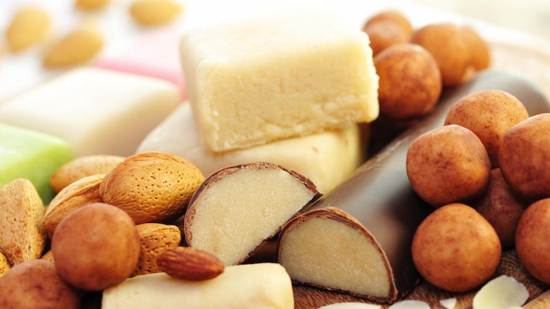 An assortment of marzipan treats, including almond-shaped pieces, chocolate-coated marzipan, round marzipan balls, and whole almonds arranged closely together.