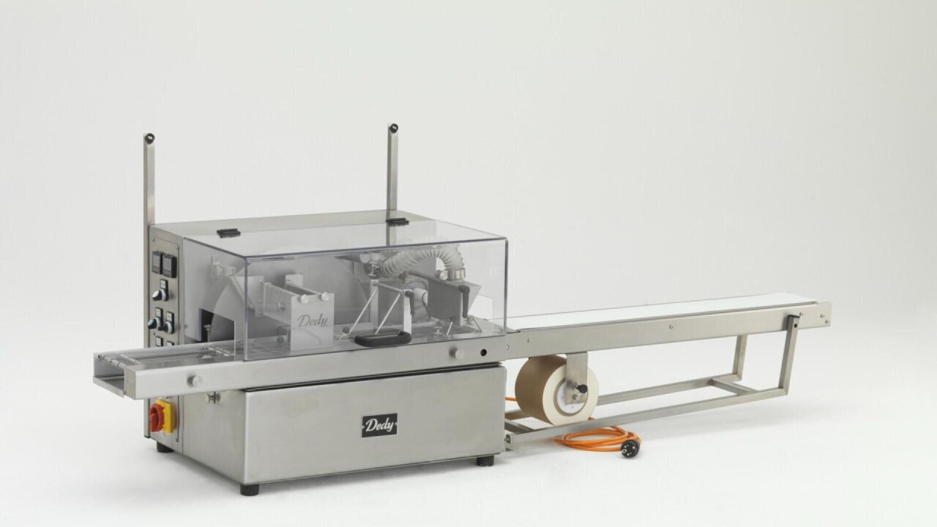 A stainless steel industrial packaging machine with a transparent cover, control buttons, a conveyor belt, and an orange power cord, set against a plain white background.