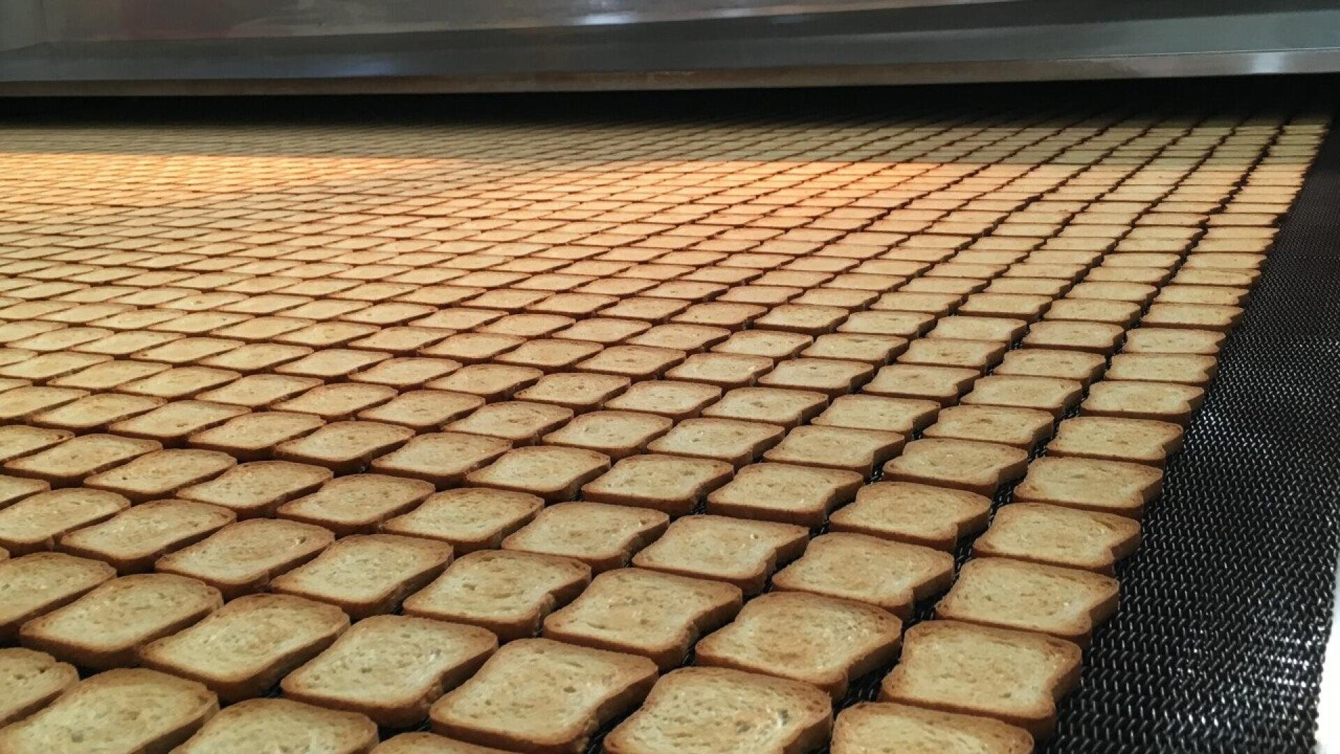 Hunderte von quadratischen Crackern oder Toastscheiben werden in einer Lebensmittelfabrik in ordentlichen Reihen auf einem Fließband angeordnet und zum Backen in einen großen Industrieofen geschoben.