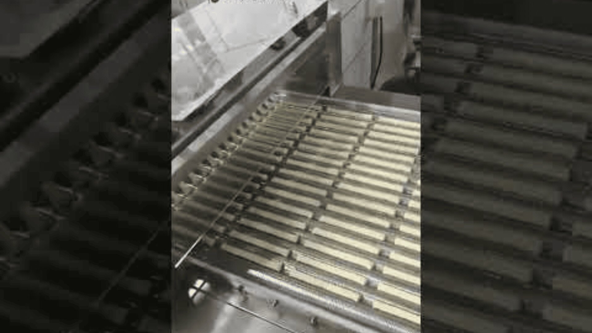 A factory machine produces even rows of rectangular cookie bars and aligns them neatly on a metal conveyor belt for processing or packaging.