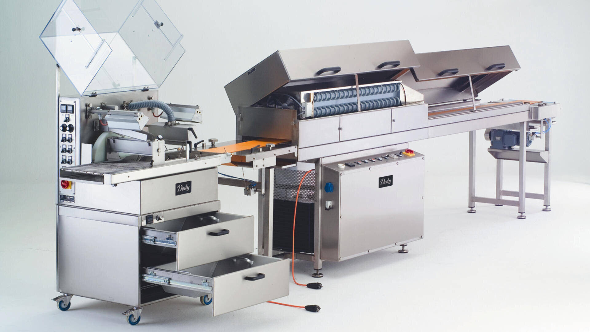 Eine industrielle Bäckereimaschine aus rostfreiem Stahl mit Förderbändern, Schalttafeln, offenen Oberteilen und Schiebeschubladen, die für die automatisierte Verarbeitung von Lebensmitteln verwendet wird, vor einem schlichten weißen Hintergrund.