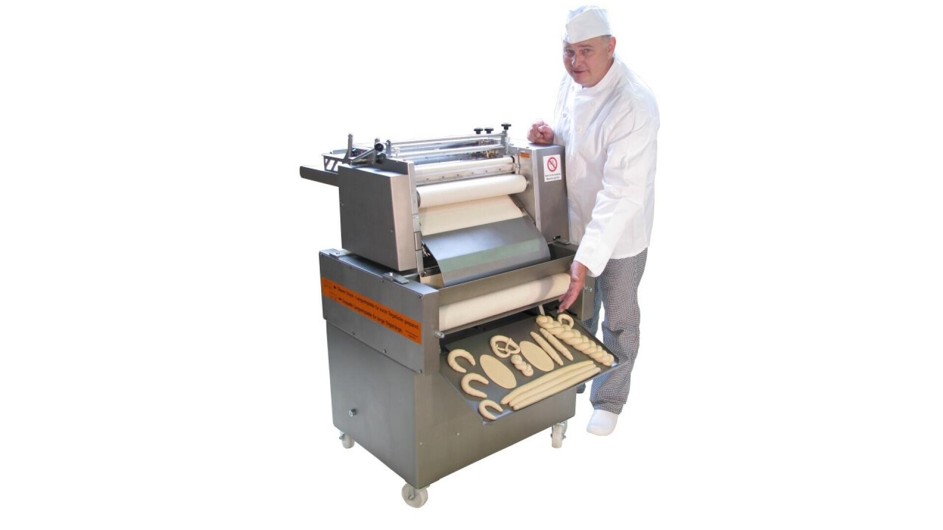 A baker in white uniform and hat stands beside a dough rolling machine, pulling out a tray filled with various shaped unbaked dough pieces. The background is plain white.