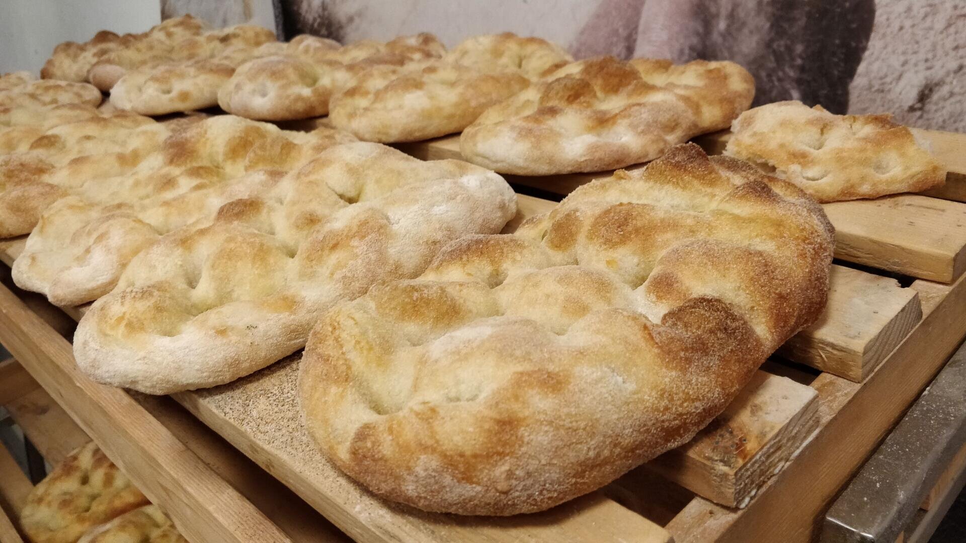 Several pieces of golden-brown, freshly baked flatbread are cooling on wooden racks, arranged side by side in rows. The bread has a rustic appearance with uneven, dimpled surfaces.