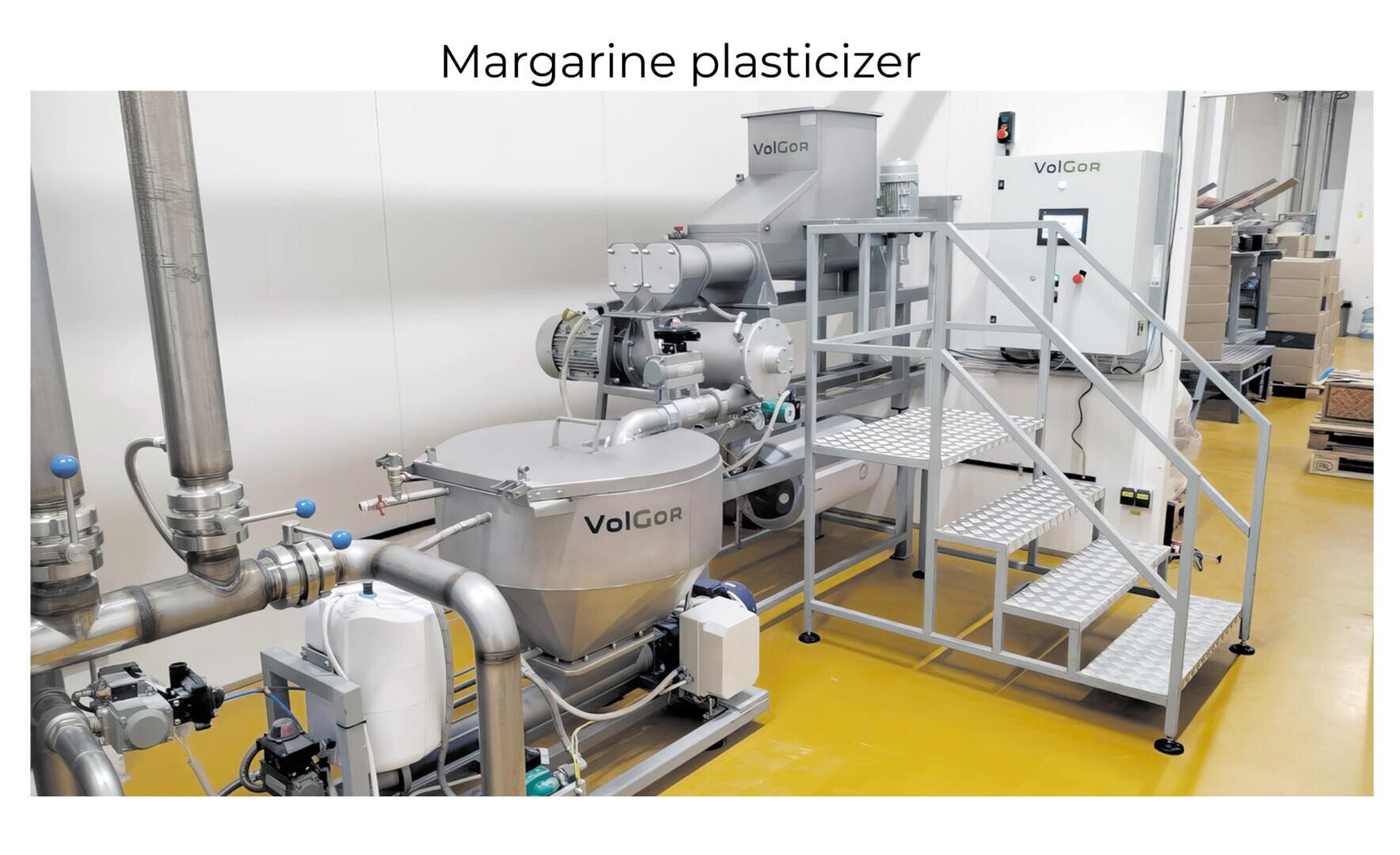Eine moderne industrielle Margarine-Weichmachermaschine mit Metalltanks, Rohren und einer Treppe steht auf gelbem Boden in einer sauberen Produktionsanlage. Das VolGor-Logo ist auf der Anlage sichtbar.