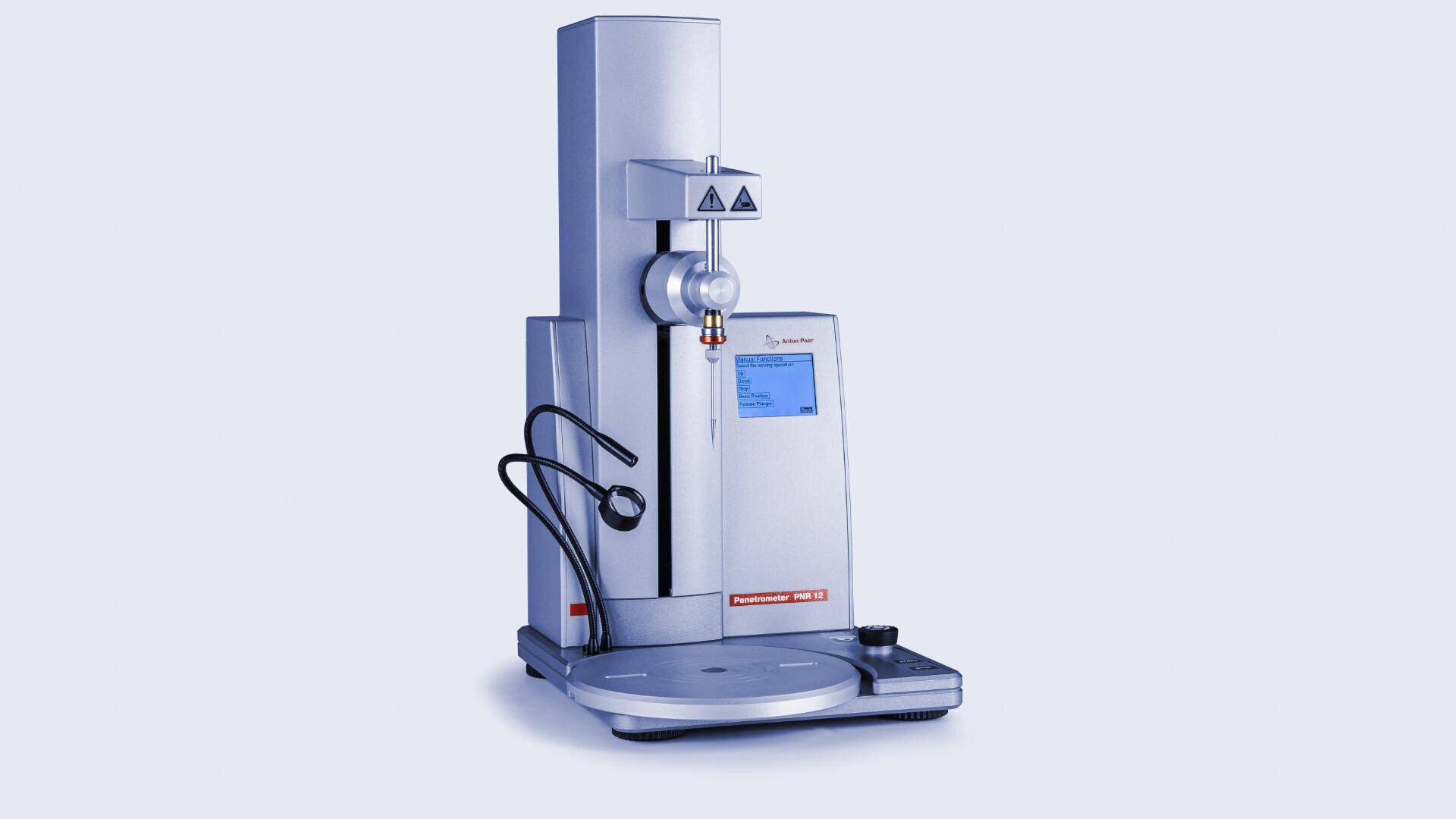 A silver laboratory instrument with a digital display and round base, used for measuring material properties, stands against a light background. Black cables are attached to the left side.