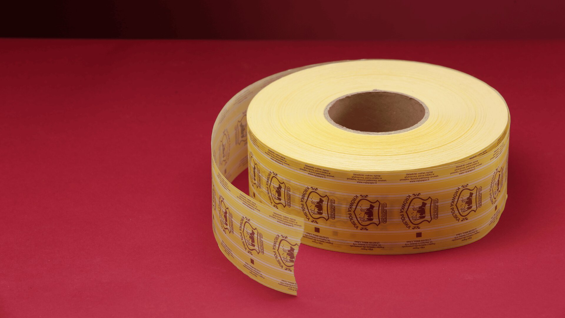 A large roll of yellow adhesive labels with printed designs sits on a red surface, with part of the roll unwound.